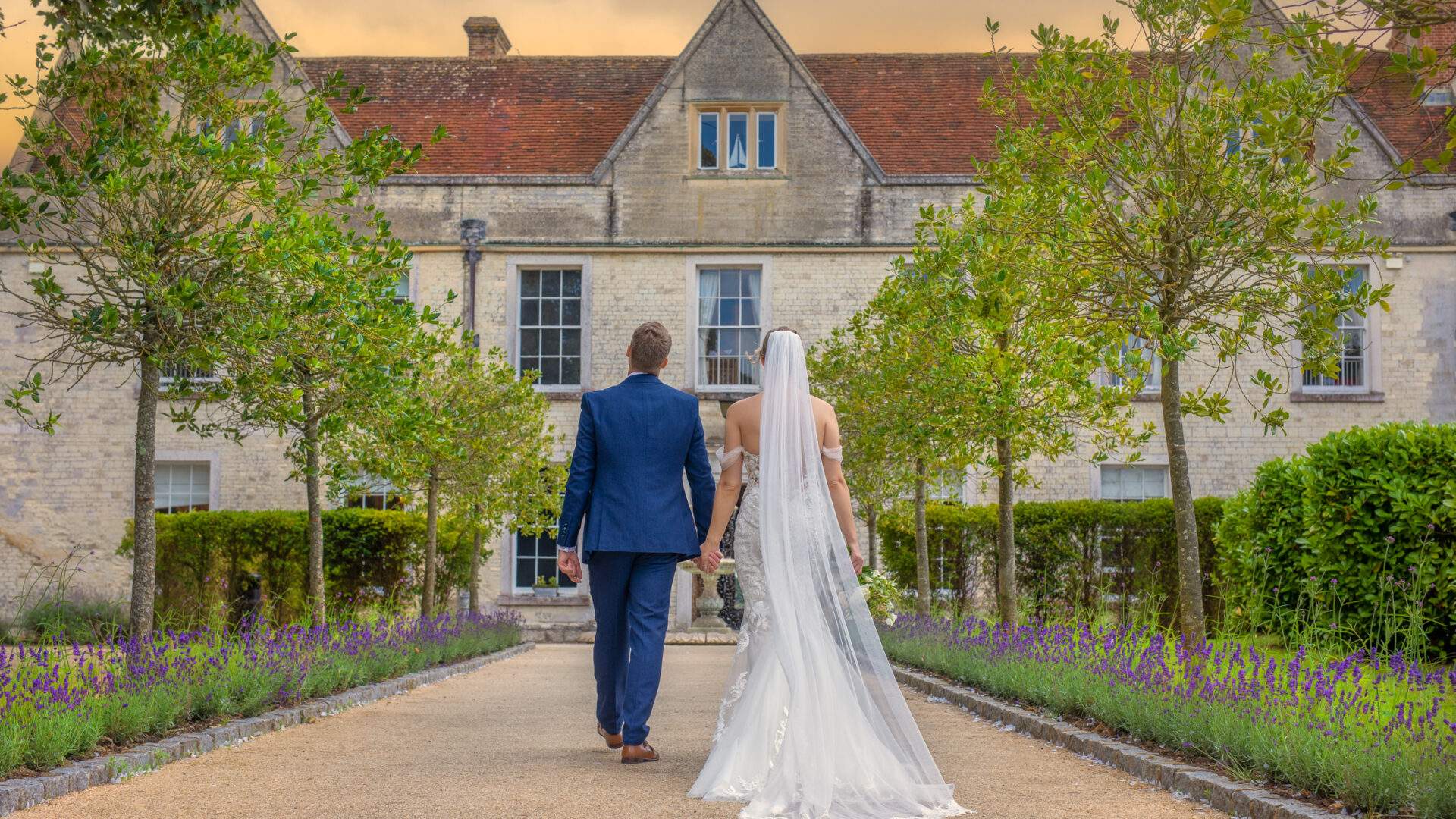 A couple walking down the grand tree lined entrance at Russets, an exclusive use wedding venue in Hampshire