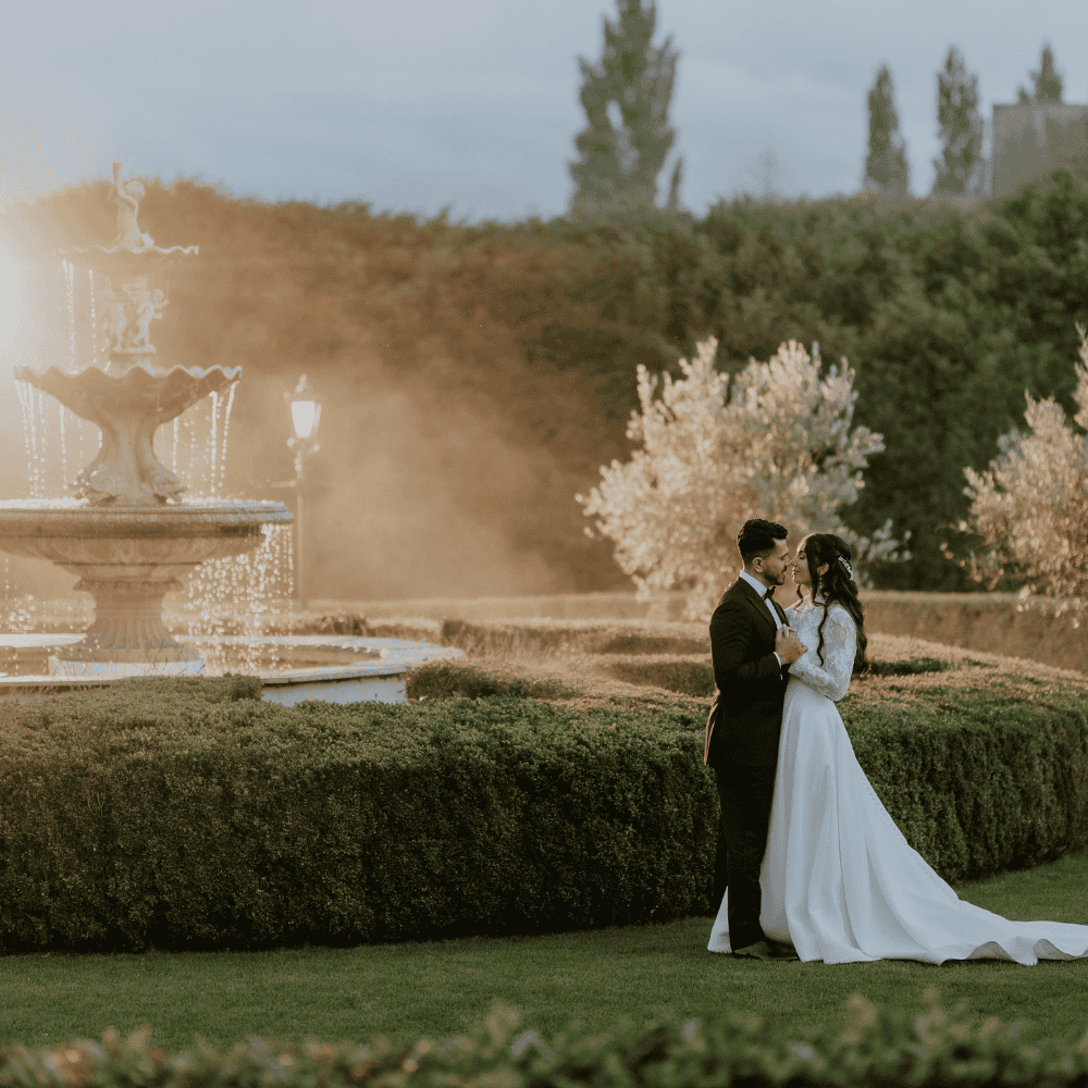 Following an outfit change into black tie, an Asian Bride & Groom pose for photos in the grounds of Russets beside the ornate water fountain.
